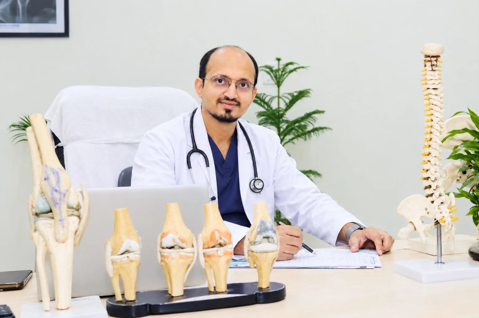 Dr. Abu Akrama at his consulting desk with knee and spine models